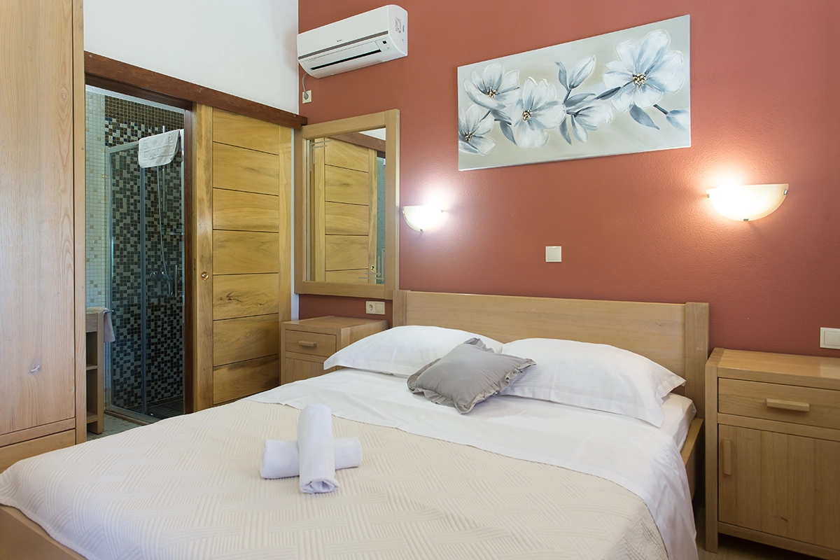 Room with an en-suite bathroom (WC), a double bed, air conditioning, a red wall, and wooden wardrobes.